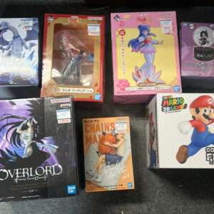 Assorted boxed anime action figures arranged on a dark carpet, including Overlord, Mario Collection Figure box, and several colorful character boxes on a shelf edge.  Articulos Japan (Post Box Japan)