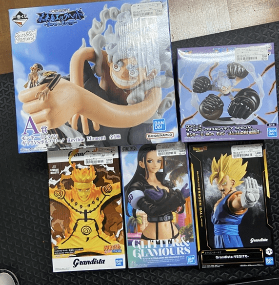 Captura De Pantalla 2026-05-04 a Las 163353 2 - Articulos Japan (post Box Japan) Boxed Bandai anime figures on display: a large One Piece Luffy figure in the top left with a giant raised fist, plus other characters in colorful boxes (Naruto/DBZ-style lineups) in the lower row; packaging shows branding like Grandista and Glitter & Glamours. Articulos Japan (Post Box Japan)