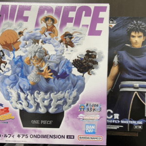 Boxed One Piece figure set with characters bursting from waves, title 'ONE PIECE' and Bandai Namco branding visible on a purple background.