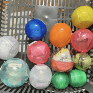 Assorted colorful plastic capsules in a gray shopping basket, including blue, yellow, orange, pink, and green.