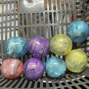 Assorted colorful plastic capsule toys in a gray shopping basket.