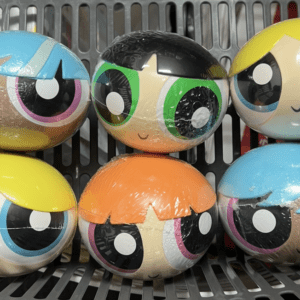 Six colorful LOL Surprise balls with big cartoon eyes in a gray basket/bin.