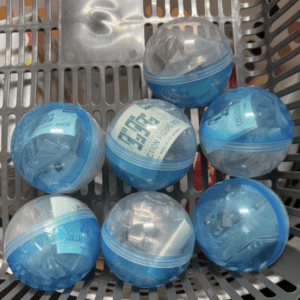 Six blue plastic capsule toys in a gray basket, each in a transparent half-shell.