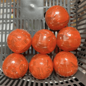 Six orange translucent toy balls with printed patterns resting in a gray plastic crate/ basket.