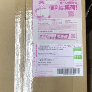Cardboard box with a large pink delivery label featuring a courier illustration, Japanese text, and a barcode/QR area.