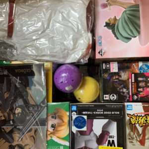 Boxed anime figures and toy boxes arranged on a shelf, with purple and yellow balls in the middle and a large wrapped item on top left making the display cluttered in a store shelf view.