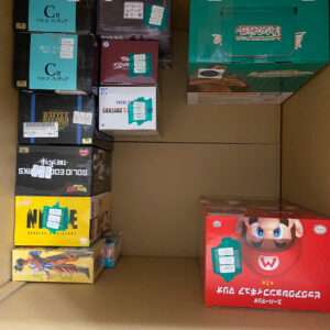 Storage shelf filled with boxed figure collectibles, including a bright red Mario box on the bottom right and various Japanese-label boxes on the left.