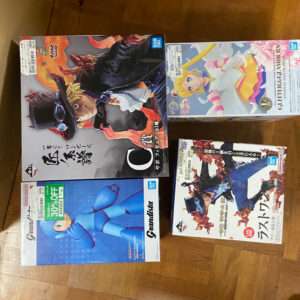 Four Bandai action-figure boxes placed on a wooden floor: a large left box with fiery artwork, a Sailor Moon box on the top right, a blue Mega Man–style figure box on the bottom left, and a fighting-character box on the bottom right.