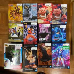 A grid of 12 boxed figures from anime and games displayed on a wooden floor, arranged in four rows of three boxes each.