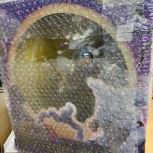 Purple boxed toy or decorative item wrapped in bubble wrap on a store shelf; shows a circular beige ring and colorful illustration behind the wrap.