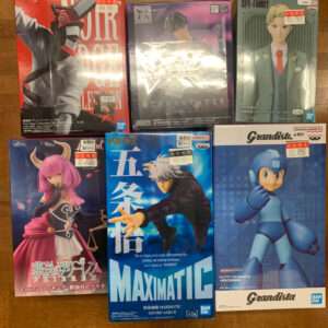Six boxed anime figures on a wooden floor, featuring colorful character designs and packaging from various brands.