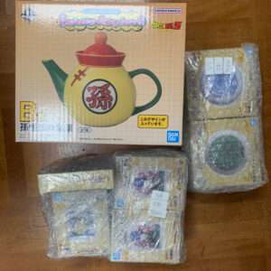Boxed Dragon Ball teapot set featuring a yellow pot with green handle and red lid, Japanese characters on front, surrounded by wrapped boxes.