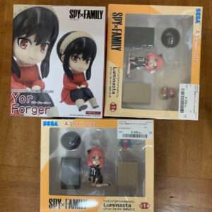Box set of SPY×FAMILY Luminsta figures on a wooden table: a large Yor Forger Relax figure box on the left, two windowed boxes with pink-haired characters on the right and bottom.