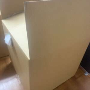Large brown cardboard box corner in a room, with a small note attached to the side and packing tape visible.
