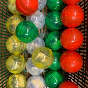 Assorted translucent toy capsules in red, green, yellow, and clear inside a green basket.