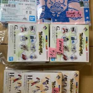 Assorted Dragon Ball merchandise: a pink towel with a blue cartoon face design and two boxed sets of 'The Chronicles of Goku' figures, with pink price notes attached, all sealed in plastic.