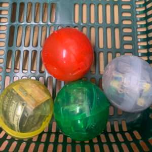 Four translucent plastic balls in a green shopping basket: red, yellow, green, and clear colors visible.