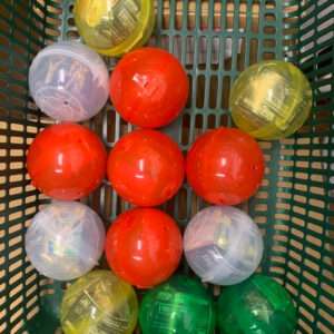 Assorted colored plastic toy capsules (red, yellow, green, and translucent) arranged in a green basket.