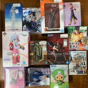 Top-down view of a wooden floor with many boxed anime figures in various colors and sizes stacked together on display shelf space (figures inside).