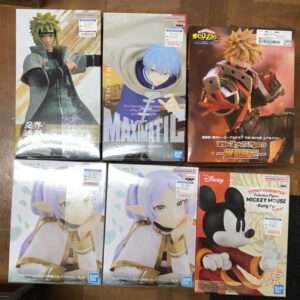 Six boxed anime figures on a wooden surface: Naruto Uzumaki in a black jacket on the left, blue-haired character in the center, orange-haired Bakugou in action on the right top edge.