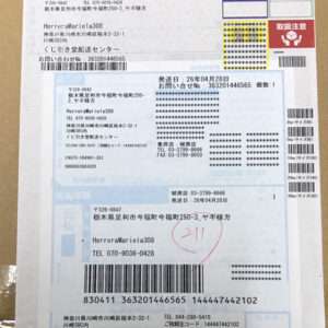 Layered Japanese shipping label with multiple sections, barcodes, tracking numbers, and a red handwritten circle stamp on a brown background.