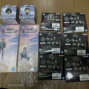 Collection of boxed anime figures on a wooden floor: two small chibi boxes top left and several black figure boxes to the right, all unopened or display backs visible.