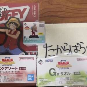 Merchandise set featuring One Piece items: large red Luffy poster, small figure box, canvas with Japanese writing, and two prize cards from Bandai Namco.