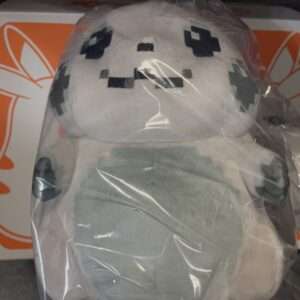 Gray plush stuffed toy with a pixelated black face pattern, wrapped in clear plastic on a store shelf Bordering an orange box.