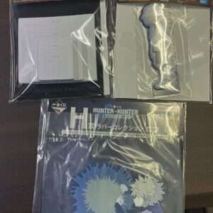 Three sealed Hunter x Hunter Zaoldyec Family memorabilia packs: left shows a white card with a maze-like geometric pattern inside a black frame; middle features a light-gray cutout piece with a character silhouette on a white backing; bottom pack displays a dark folder with anime artwork and a blue gear motif.