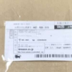Brown cardboard box with a white shipping label on top, featuring a barcode and small printed text (label is somewhat blurred).