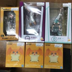 Assorted boxed figures on a wooden shelf: three large windowed boxes on top (orange, purple, and teal) and three orange character boxes below.