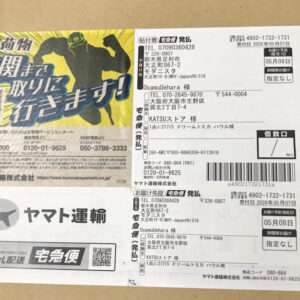 Cardboard box with Japanese shipping labels and a Yamato Transport logo on the left; colorful ad banner on top-left corner.