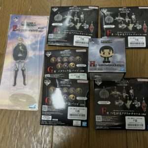 Assorted Bandai Namco collectible boxes and a tall character standee on a wooden floor, featuring acrylic charms and figures from an anime set.