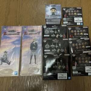 Assorted Attack on Titan acrylic stands and badge boxes laid out on a wooden floor.