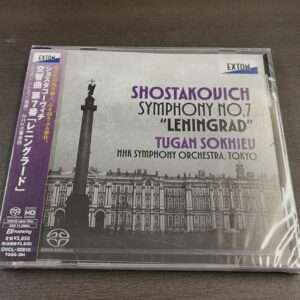 CD case cover for Shostakovich Symphony No. 7 'Leningrad' with NHK Symphony Orchestra Tokyo; features a grayscale cityscape and a tall monument, purple Japanese obi band on left edge.