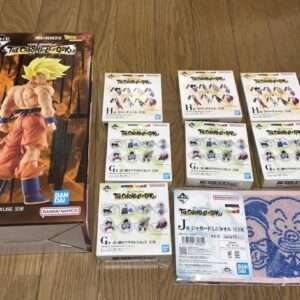 Boxed Dragon Ball Z Goku figure on the left; multiple Chronicles of Goku boxes arranged on a wooden floor, with a pink cartoon towel on the right.
