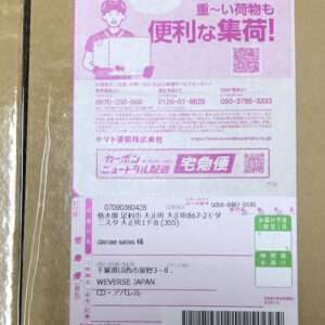 Cardboard box with a large pink Japanese shipping label featuring a courier illustration, QR codes, and a barcode on the package.