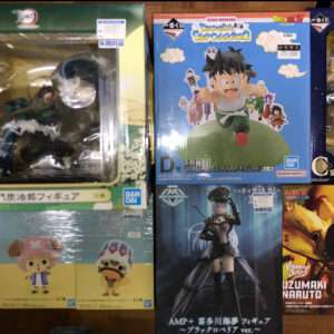 A collection of Japanese anime action-figure boxes laid out on a wooden surface, featuring Dragon Ball, Naruto, and other characters.