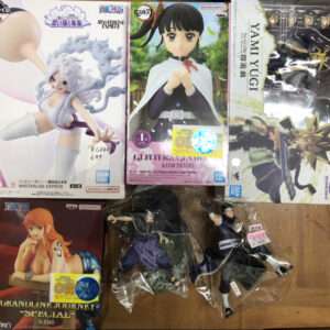 Assorted boxed anime figures laid on a wooden floor, including Demon Slayer's Kanao Tsuyuri and Yu-Gi-Oh characters among others.