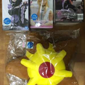 Three boxed anime figures lined up on a wooden floor, with a large yellow sun-shaped plush in plastic below them on the right.