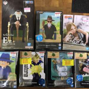 Row of boxed anime figurines on a wooden floor, including The Throne of Power E prize figure and several character Figures in colorful packaging (Naruto, Dragon Ball, etc.).