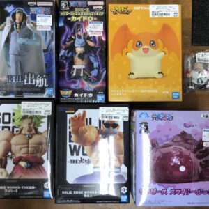Assorted Bandai action figure boxes on a wooden table, featuring Dragon Ball and One Piece characters among others.