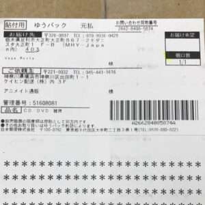 Japanese shipping label on brown cardboard showing sender/recipient addresses, phone numbers, and a large barcode; small delivery preference box visible.