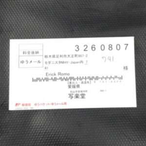 White mailing label on a dark textured surface showing recipient 'Erick Romo', address lines, a large number 3260807, and a barcode-like stripe.  Articulos Japan (Post Box Japan)