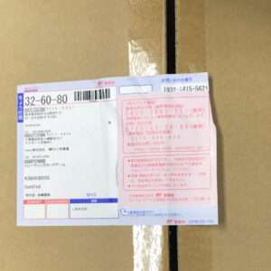 Cardboard box with a blue and pink Japanese postal label showing a barcode and tracking number.