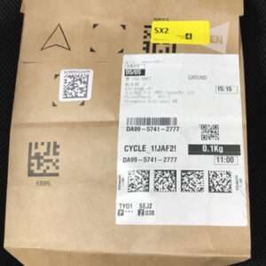Brown cardboard parcel with a white shipping label, barcodes and QR codes, and a yellow SX2 sticker on the top edge.