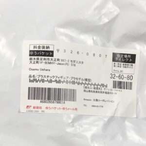 Delivery label on a white plastic bag, with Japanese text, a barcode, and postal/tracking numbers.