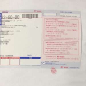 Blurry photo of a Japanese delivery form with a barcode in the top-left, text blocks on the left, and pink notice boxes on the right.  Articulos Japan (Post Box Japan)