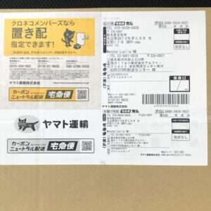 Brown cardboard box covered with Japanese shipping labels, barcodes, and Yamato Transport logos, including a yellow label with a cat icon.