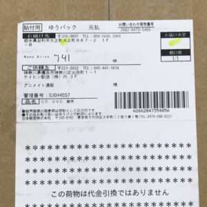 Delivery label on a brown cardboard box with recipient info, a barcode, and a bold notice: 'この荷物は代金引換ではありません' (not cash on delivery).